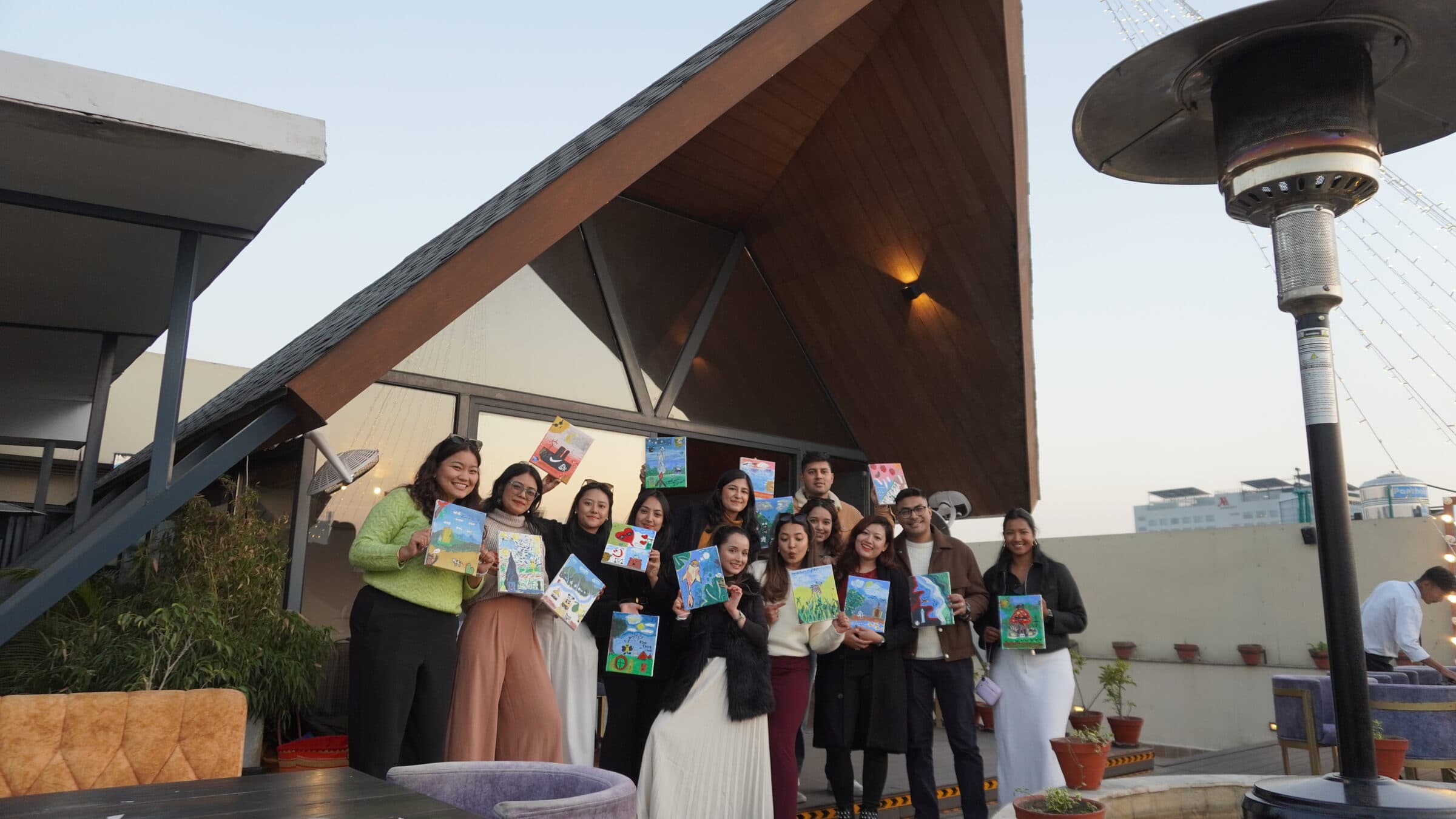 The first eighteen guests of The Guest List, around one table, holding their canvases